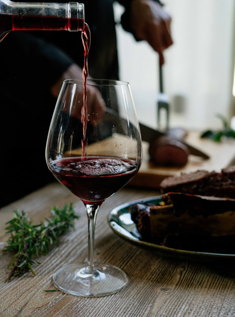 Rödvin hälls i ett glas vid en elegant dukning